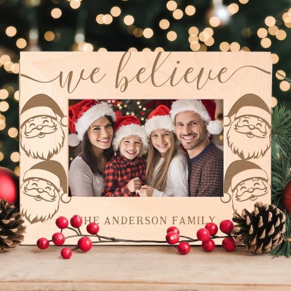 Wooden Christmas Photo Frame With Santa Faces And The Words We Believe. A Family Photo Is Inside.