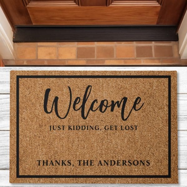 Tan Welcome Mat With Black Border And Text That Says Welcome, Just Kidding, Get Lost, And Thanks, The Andersons.