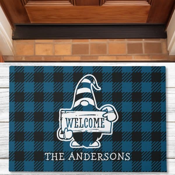 Welcome Mat With A Gnome Holding A Welcome Sign, On A Blue And Black Buffalo Plaid Background; The Andersons Is Printed Below.