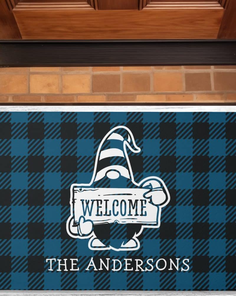 Welcome mat with a gnome holding a welcome sign, on a blue and black buffalo plaid background; The Andersons is printed below.