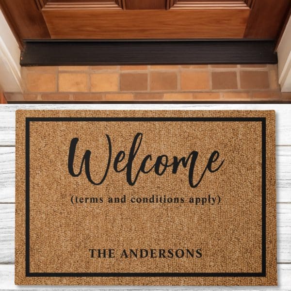 A Tan Welcome Mat With Black Text. The Words Welcome, Terms And Conditions Apply, And The Andersons Are Visible.