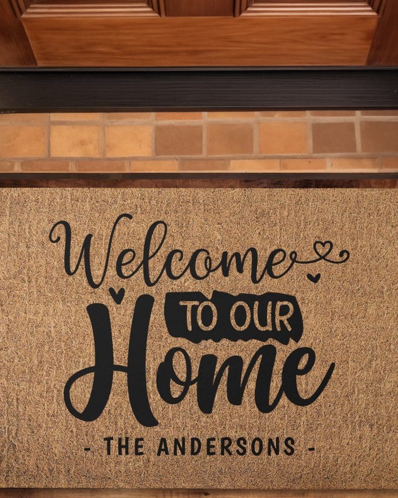 A tan welcome mat with black lettering that reads Welcome to Our Home, The Andersons.