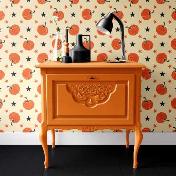 Orange Painted Dresser With Ornate Detailing, Holding A Lamp And Decorative Objects, Against A Wall With A Pumpkin And Star Pattern.