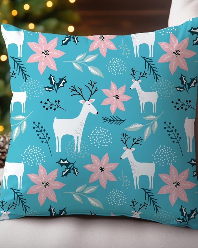 Teal decorative pillow with a repeating pattern of white reindeer and pink poinsettias.