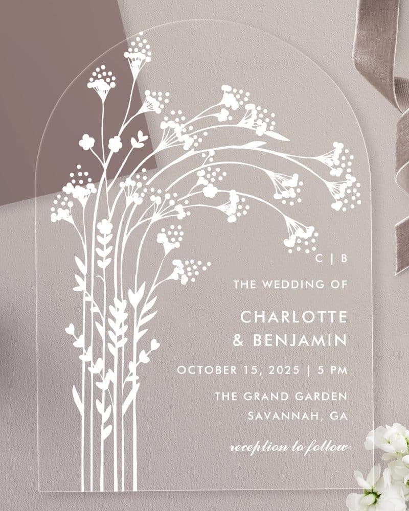 Clear acrylic wedding invitation with white floral design and wedding details.