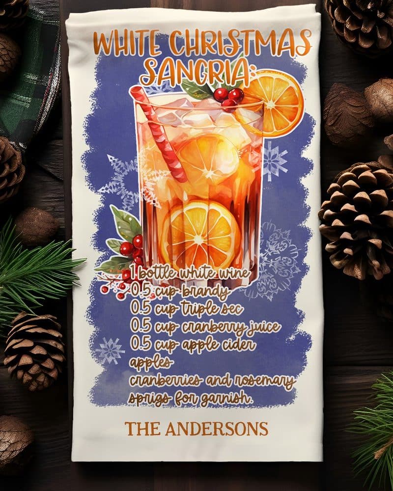 White Christmas Sangria recipe on a kitchen towel, featuring an illustration of a glass of sangria with oranges and cranberries.
