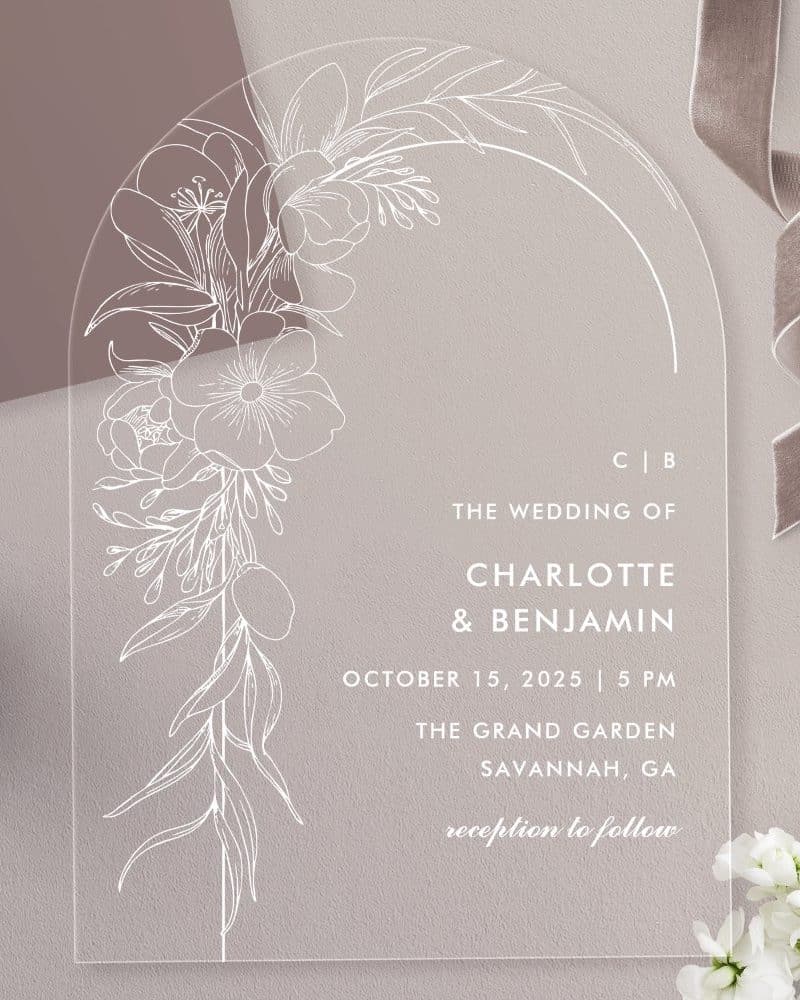 Clear acrylic wedding invitation with white floral design and wedding details.