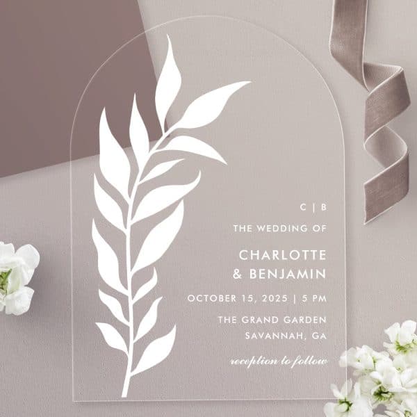Arch-Shaped Acrylic Wedding Invitation With A White Stylized Leaf Design And The Couple'S Names And Wedding Details.