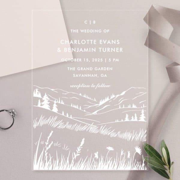 Clear Wedding Invitation With White Line Art Of Rolling Hills, Trees, And Grass. The Couple'S Names And Wedding Details Are Printed On The Invitation.