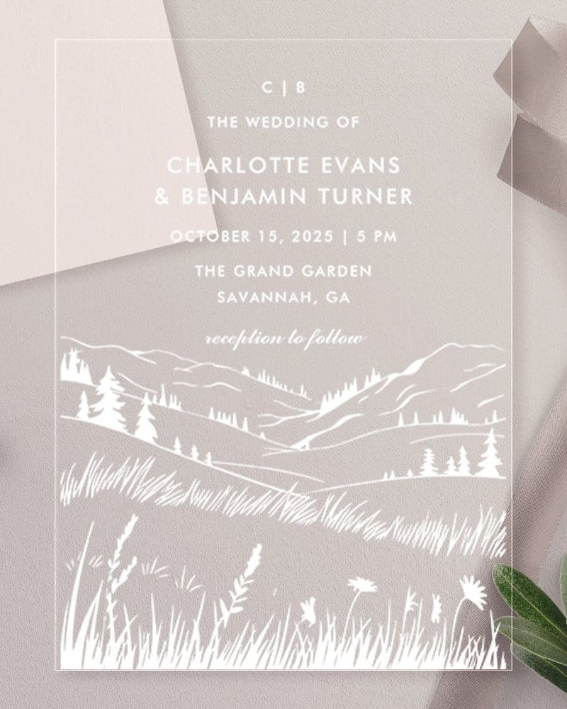 Clear wedding invitation with white line art of rolling hills, trees, and grass. The couple's names and wedding details are printed on the invitation.