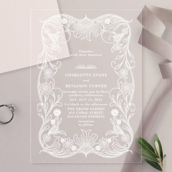 Clear Acrylic Wedding Invitation With White Floral Design And Text Announcing Charlotte Evans And Benjamin Turner'S Wedding.