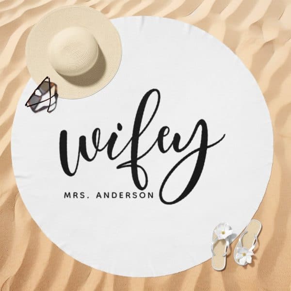 White Round Beach Towel With The Word Wifey In A Stylized Script Font And Mrs. Anderson Below It.