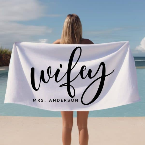 Woman Holding A White Beach Towel With The Word Wifey And Her Last Name, Anderson, Written On It.