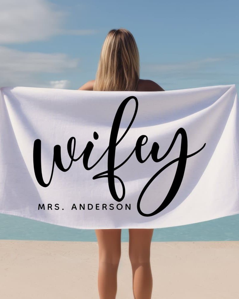 Woman holding a white beach towel with the word wifey and her last name, Anderson, written on it.