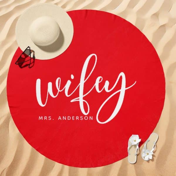 Red Round Beach Towel With The Word Wifey In White Script Lettering And Mrs. Anderson Below It.