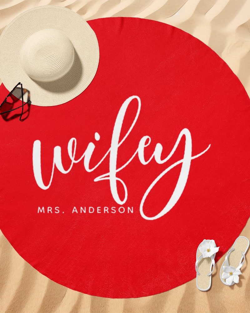Red round beach towel with the word wifey in white script lettering and Mrs. Anderson below it.