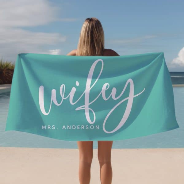 Woman Holding A Teal Beach Towel With The Word Wifey And Mrs. Anderson In White Script.
