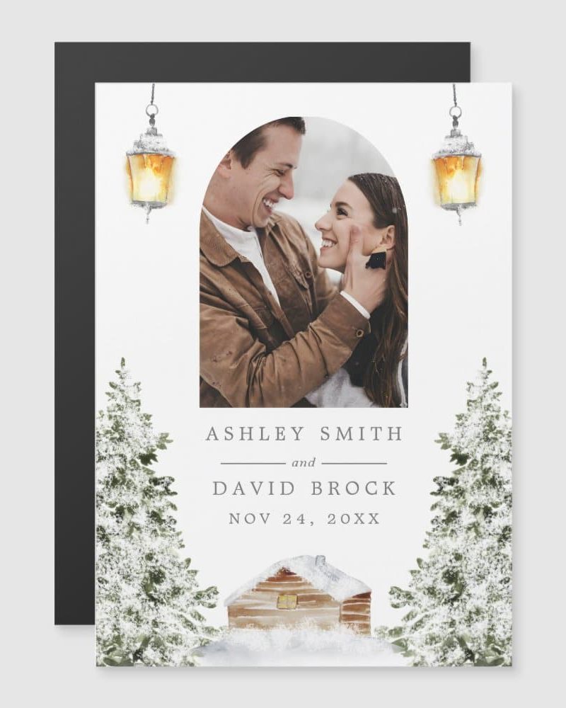 A winter wedding announcement featuring a photo of a smiling couple, snowy evergreens, a cozy cabin, and hanging lanterns.