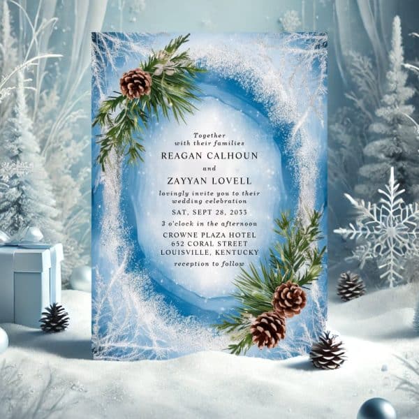 Wedding Invitation With A Winter Theme; Blue Background, Pine Branches, And Pinecones. The Names Reagan Calhoun And Zayyan Lovell Are Prominently Displayed.