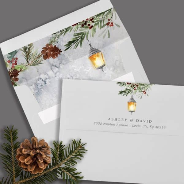 Wedding Invitation With A Winter Theme; A Lantern And Evergreen Boughs Are Featured On A Gray Envelope.