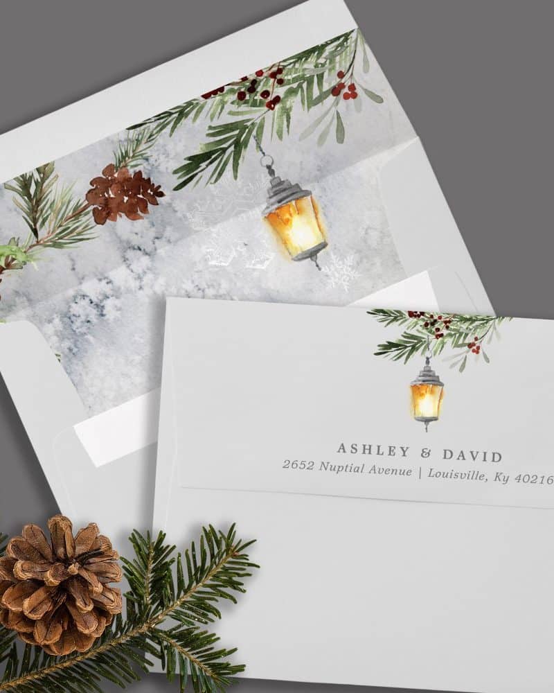 Wedding invitation with a winter theme; a lantern and evergreen boughs are featured on a gray envelope.