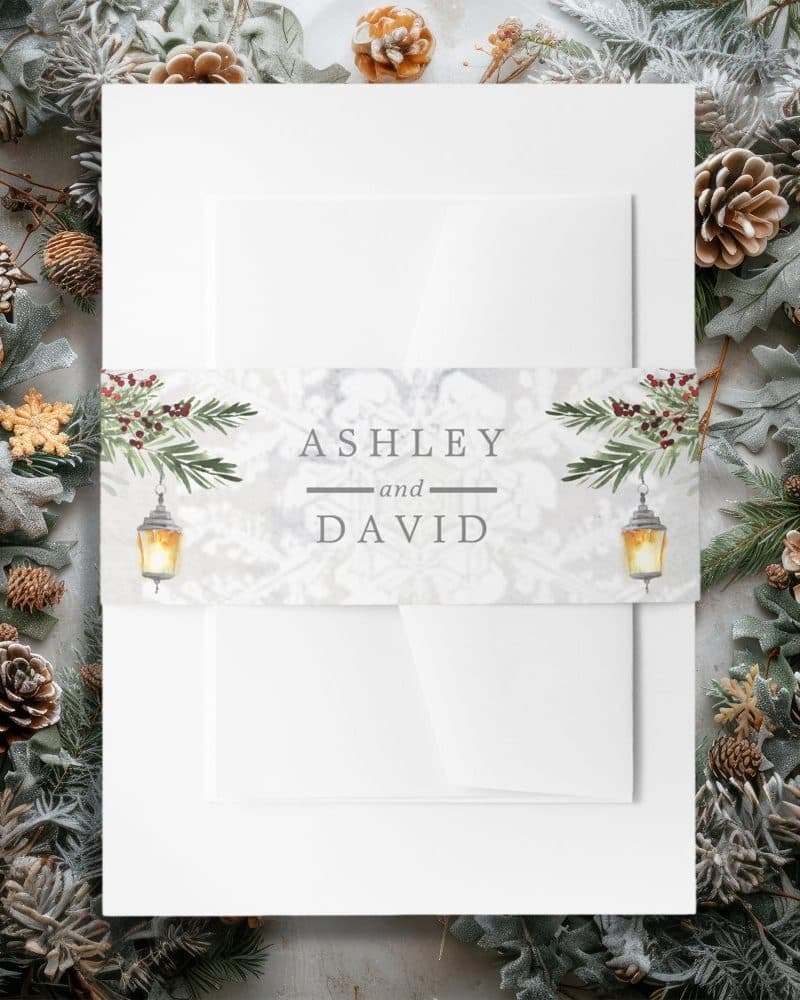 Wedding invitation with a winter theme. Names Ashley and David are displayed on a band featuring pine branches and lanterns.