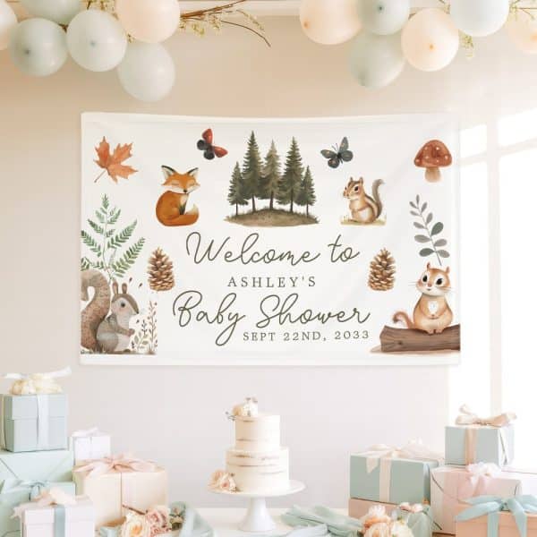 A Woodland-Themed Baby Shower Banner For Ashley, Featuring Cartoon Animals Like Foxes And Squirrels, Along With Trees And Pinecones. The Date Is Also Included.