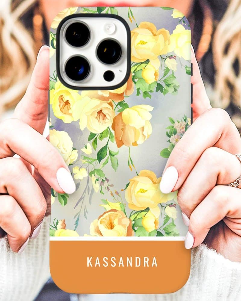 Woman's hands holding an iPhone case with a yellow floral pattern and the name Kassandra at the bottom.