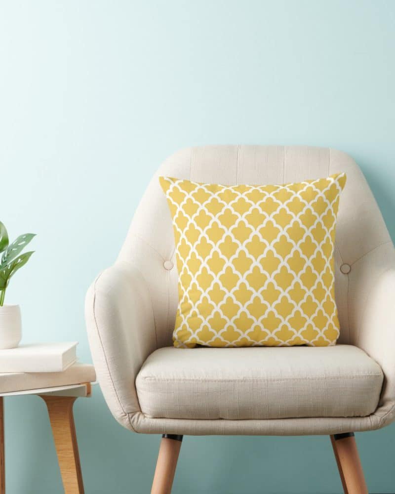 Beige armchair with a mustard yellow patterned throw pillow.