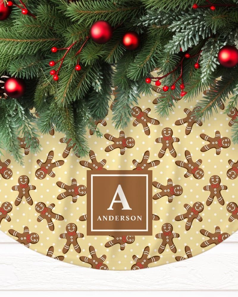 A Christmas tree skirt with a pale yellow background featuring a repeating pattern of gingerbread men and white polka dots. The skirt is personalized with the initial A and the last name Anderson.