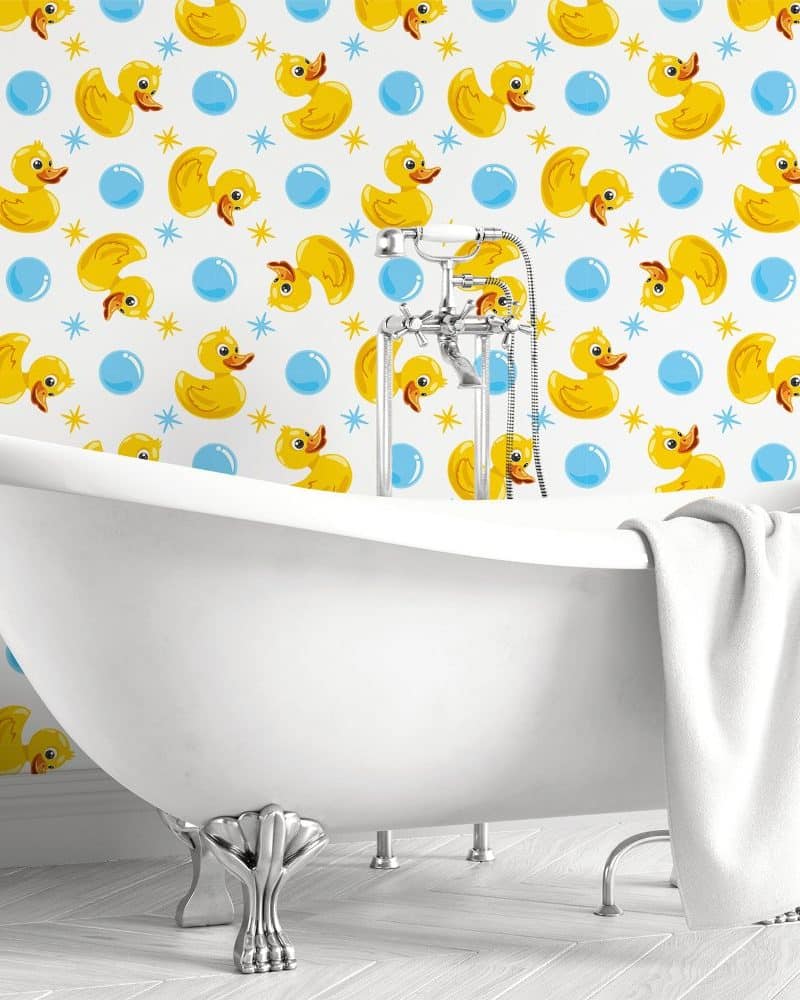 White clawfoot bathtub in front of wallpaper featuring yellow rubber ducks and blue bubbles.