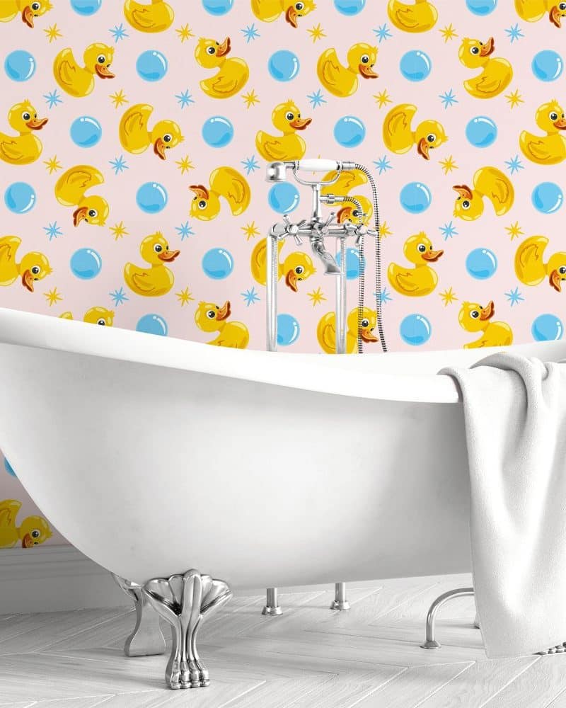 White clawfoot bathtub in a bathroom with pink wallpaper featuring yellow rubber ducks and blue bubbles.