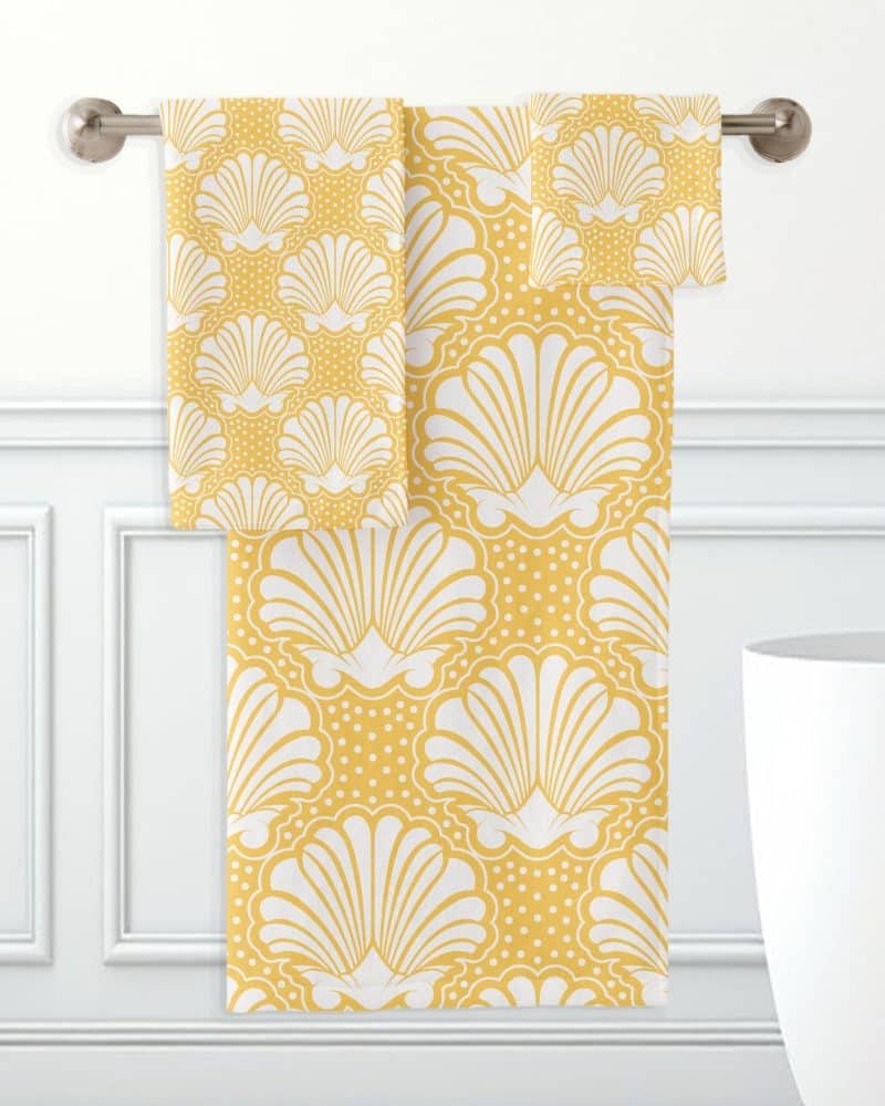 Yellow bath towels with a white seashell pattern hanging on a towel rack.