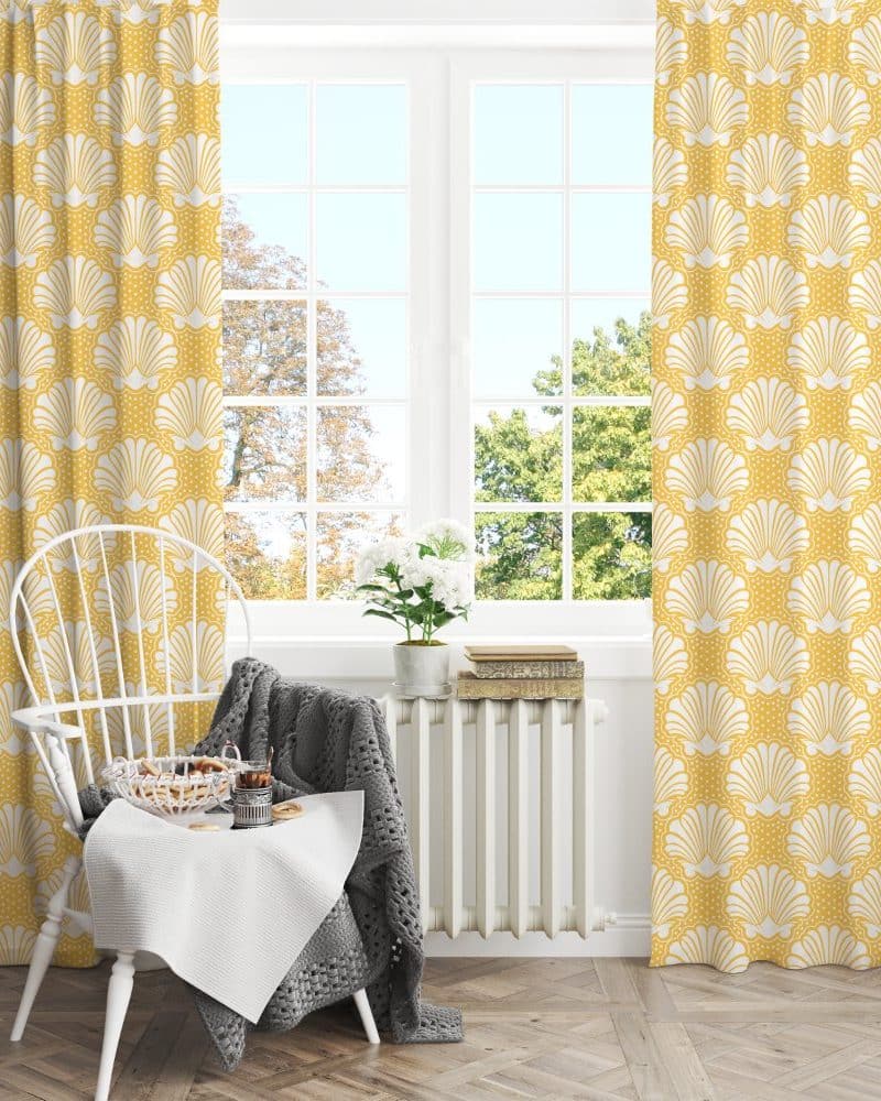 Pair of mustard yellow curtains with a white seashell pattern, hanging in a bright window.