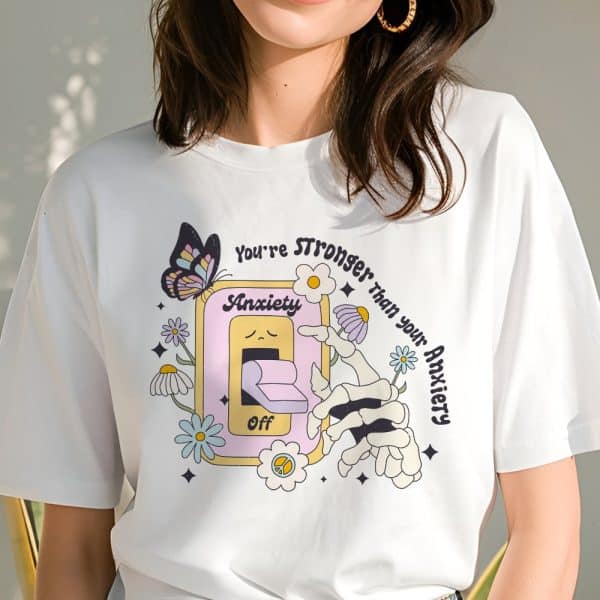 White T-Shirt With A Graphic Design Featuring A Skeleton Hand Turning Off An Anxiety Switch; Flowers And A Butterfly Are Also Included In The Design.