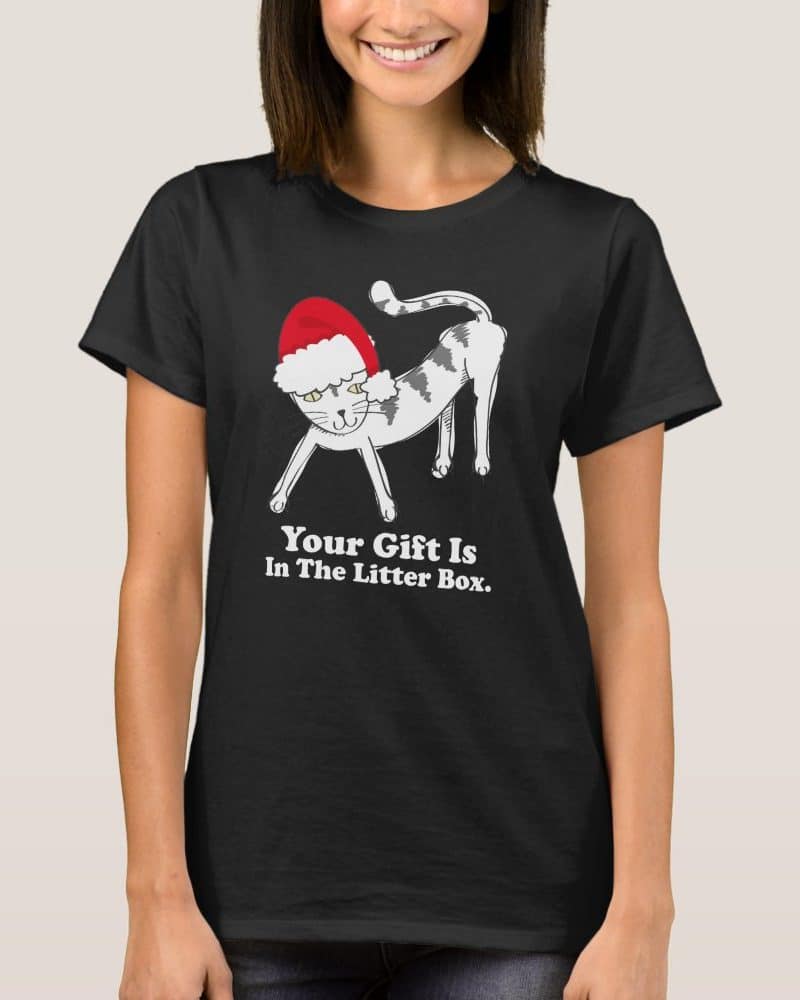 Black t-shirt featuring a cartoon cat wearing a Santa hat. Text below reads Your Gift Is In The Litter Box.