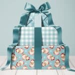 Stack of three Christmas presents tied with a teal ribbon. The bottom present features a Santa Claus pattern.