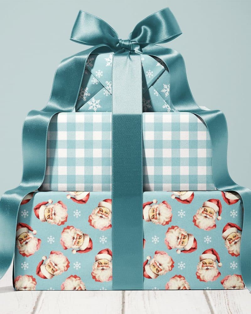 Stack of three Christmas presents tied with a teal ribbon. The bottom present features a Santa Claus pattern.