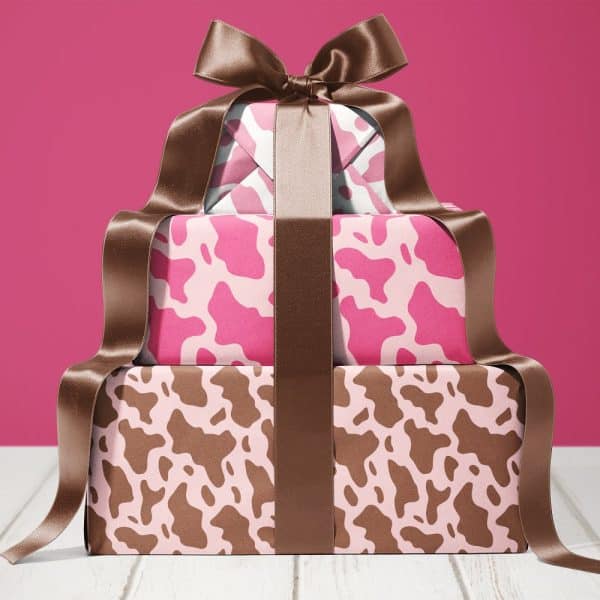 Stack Of Three Gifts Wrapped In Pink And Brown Cow Print Paper, Tied With A Large Brown Ribbon.