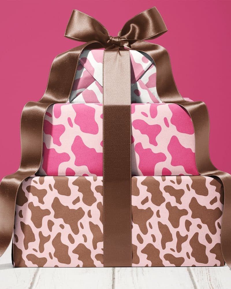 Stack Of Three Gifts Wrapped In Pink And Brown Cow Print Paper, Tied With A Large Brown Ribbon.