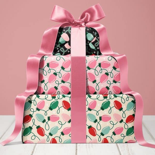 Stack Of Christmas Presents Wrapped In Lightbulb Patterned Paper And Tied With A Large Pink Ribbon.