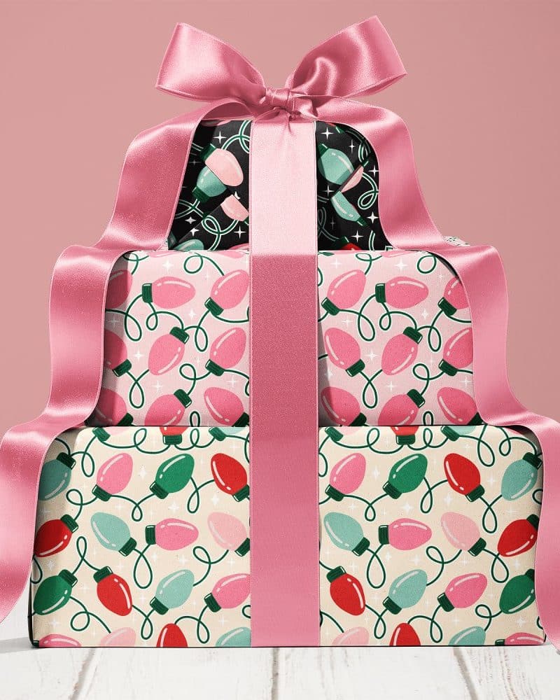 Stack of Christmas presents wrapped in lightbulb patterned paper and tied with a large pink ribbon.