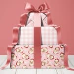 Stack of three pink Christmas presents tied with a large rose-gold ribbon.