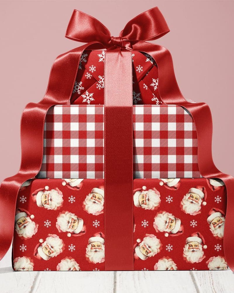 Stack of three Christmas presents wrapped in red paper with various patterns and tied with a large red ribbon.